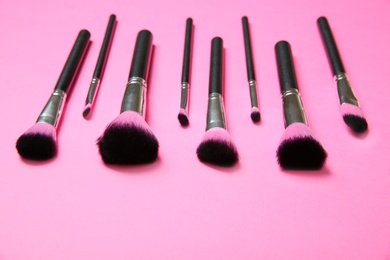 Set of professional makeup brushes on pink background