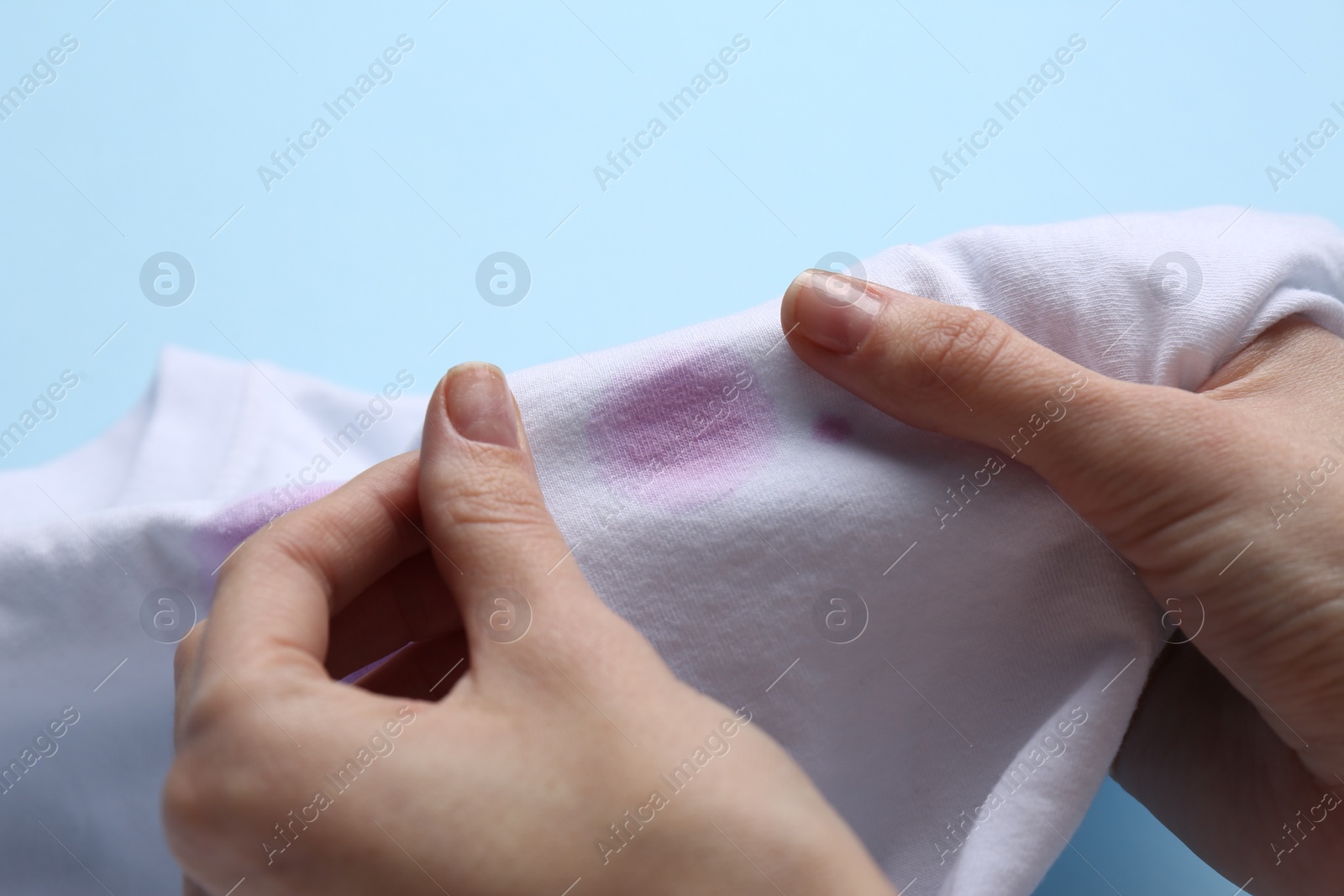 Photo of Woman holding white shirt with purple stain on light blue background, closeup