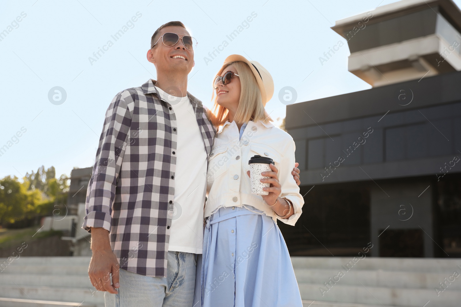 Photo of Happy couple with drink walking along city street on summer day