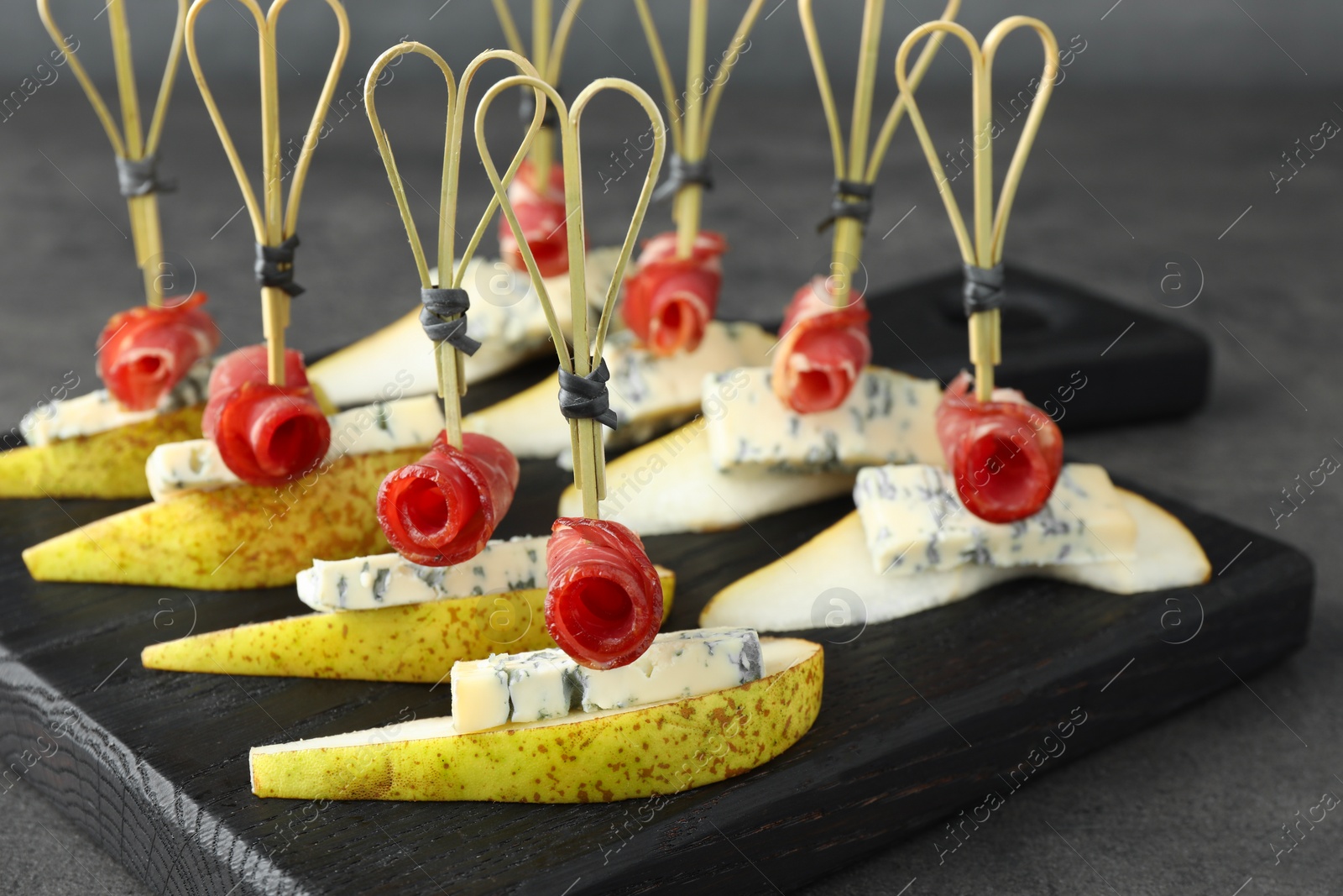 Photo of Tasty canapes with pears, blue cheese and prosciutto on grey table, closeup