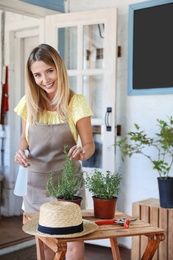 Photo of Young woman sprinkling home plants at wooden table outdoors