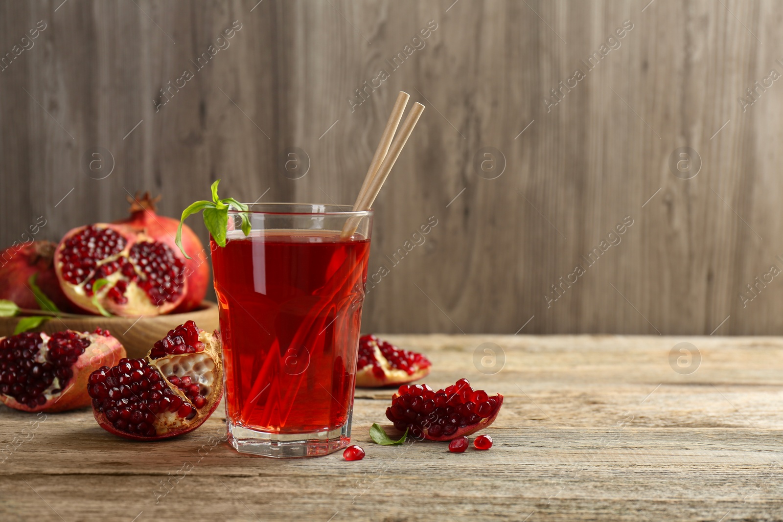 Photo of Tasty pomegranate juice in glass and fresh fruits on wooden table. Space for text