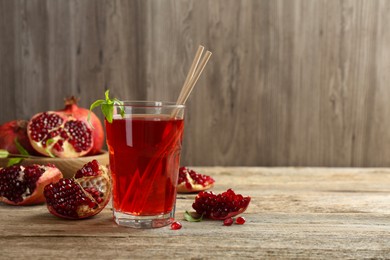 Photo of Tasty pomegranate juice in glass and fresh fruits on wooden table. Space for text