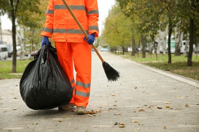 Photo of Street cleaner with broom and garbage bag outdoors on autumn day, closeup