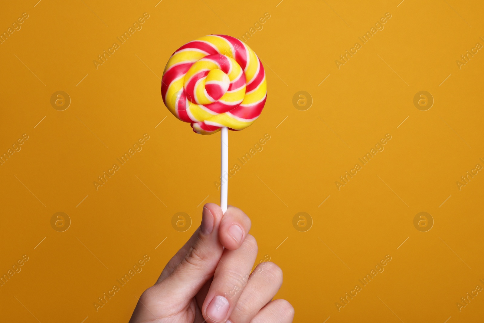 Photo of Woman holding bright tasty lollipop on orange background, closeup