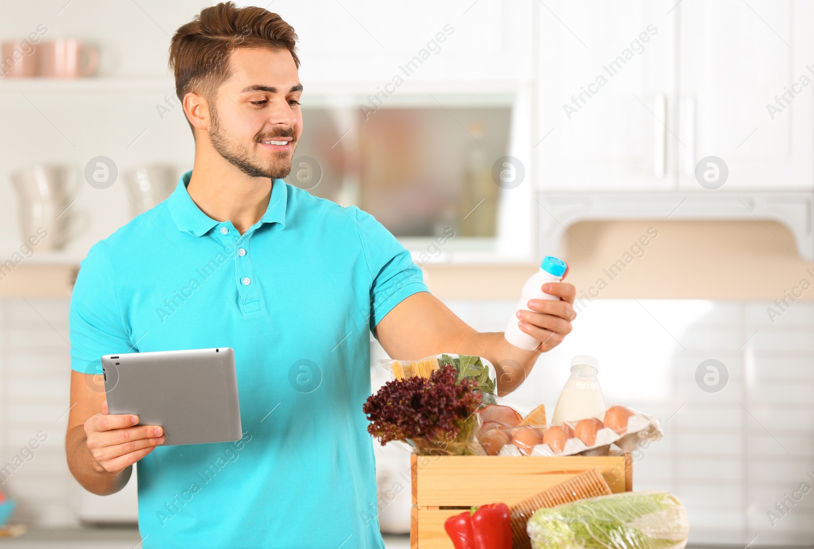 Photo of Young man with tablet PC and products in kitchen. Food delivery service