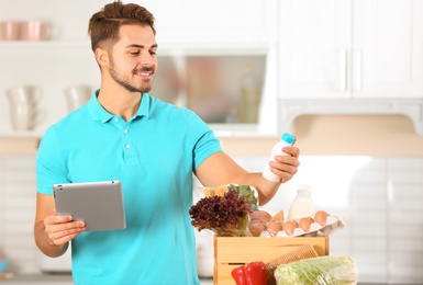 Photo of Young man with tablet PC and products in kitchen. Food delivery service