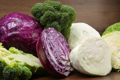 Photo of Different types of cabbage on wooden table, closeup