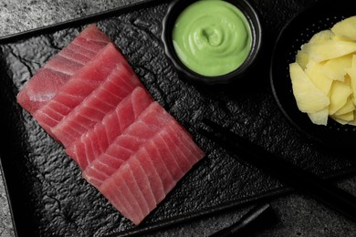 Photo of Tasty sashimi (pieces of fresh raw tuna) served with wasabi sauce and ginger slices on black plate, flat lay