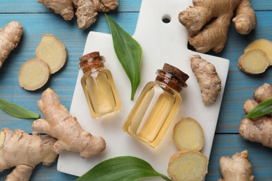 Glass bottles of essential oil and ginger root on light blue wooden table, flat lay