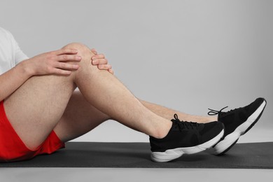 Man suffering from leg pain on mat against grey background, closeup
