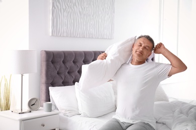 Happy man with soft pillow sitting on bed at home