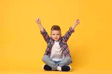 Photo of Happy little boy sitting on yellow background