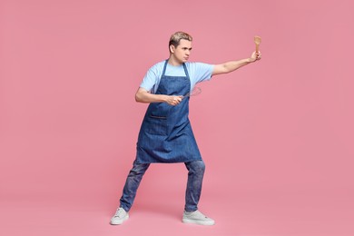 Portrait of confectioner holding spatula and whisk on pink background