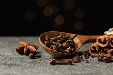Photo of Wooden spoon with different spices on gray table against black background, closeup
