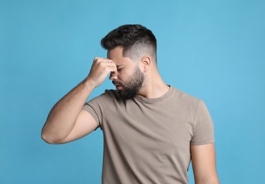 Young man suffering from headache on light blue background
