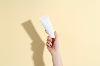 Photo of Woman holding tube of cream on yellow background, closeup