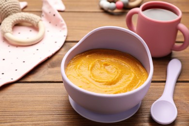 Photo of Plastic dishware with healthy baby food on wooden table