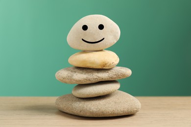 Photo of Stack of stones with drawn happy face on table against turquoise background, closeup. Zen concept