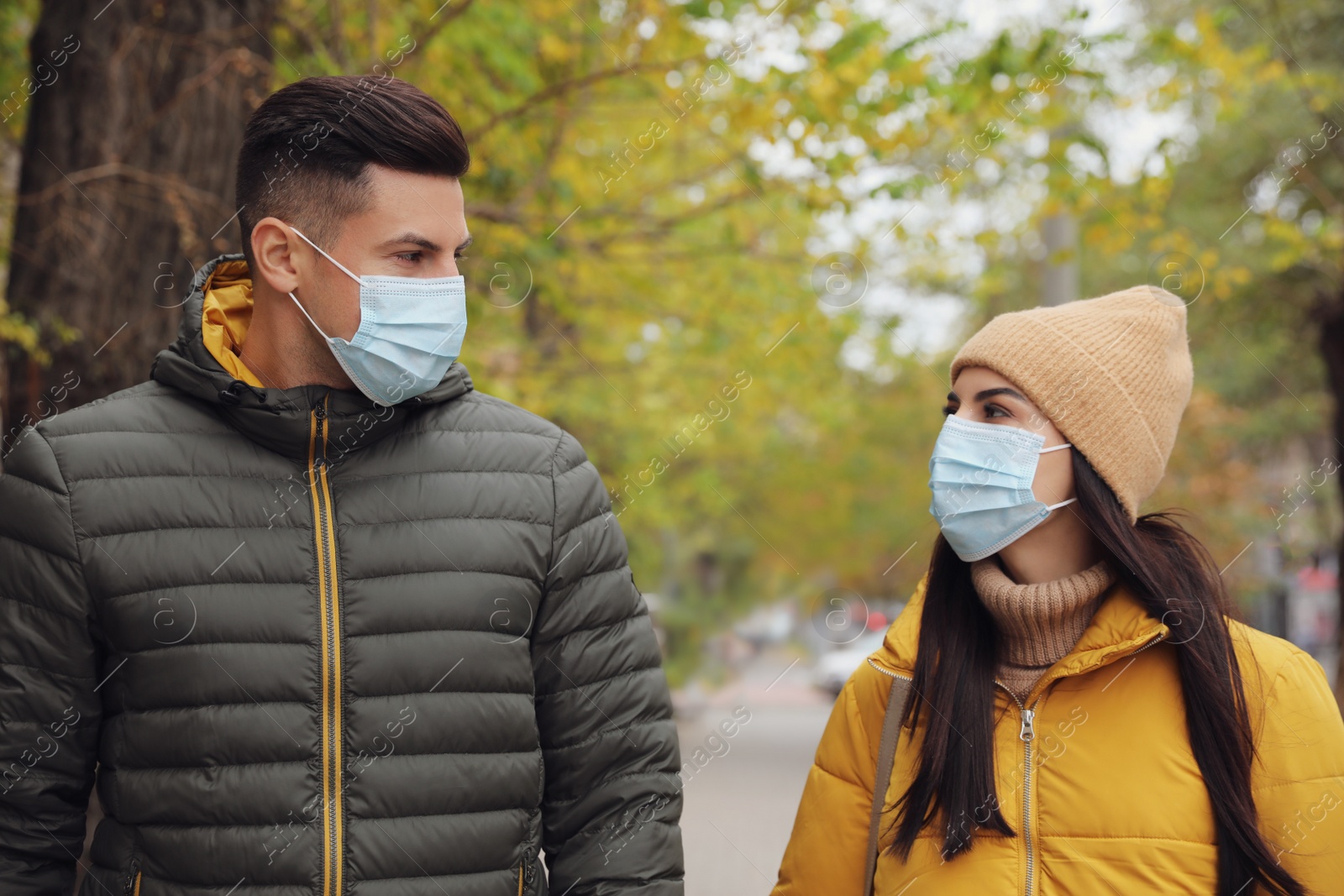 Photo of Couple in medical face masks walking outdoors. Personal protection during COVID-19 pandemic