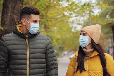 Photo of Couple in medical face masks walking outdoors. Personal protection during COVID-19 pandemic