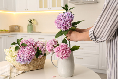 Woman making bouquet with beautiful hydrangea flowers at table indoors, closeup. Interior design element