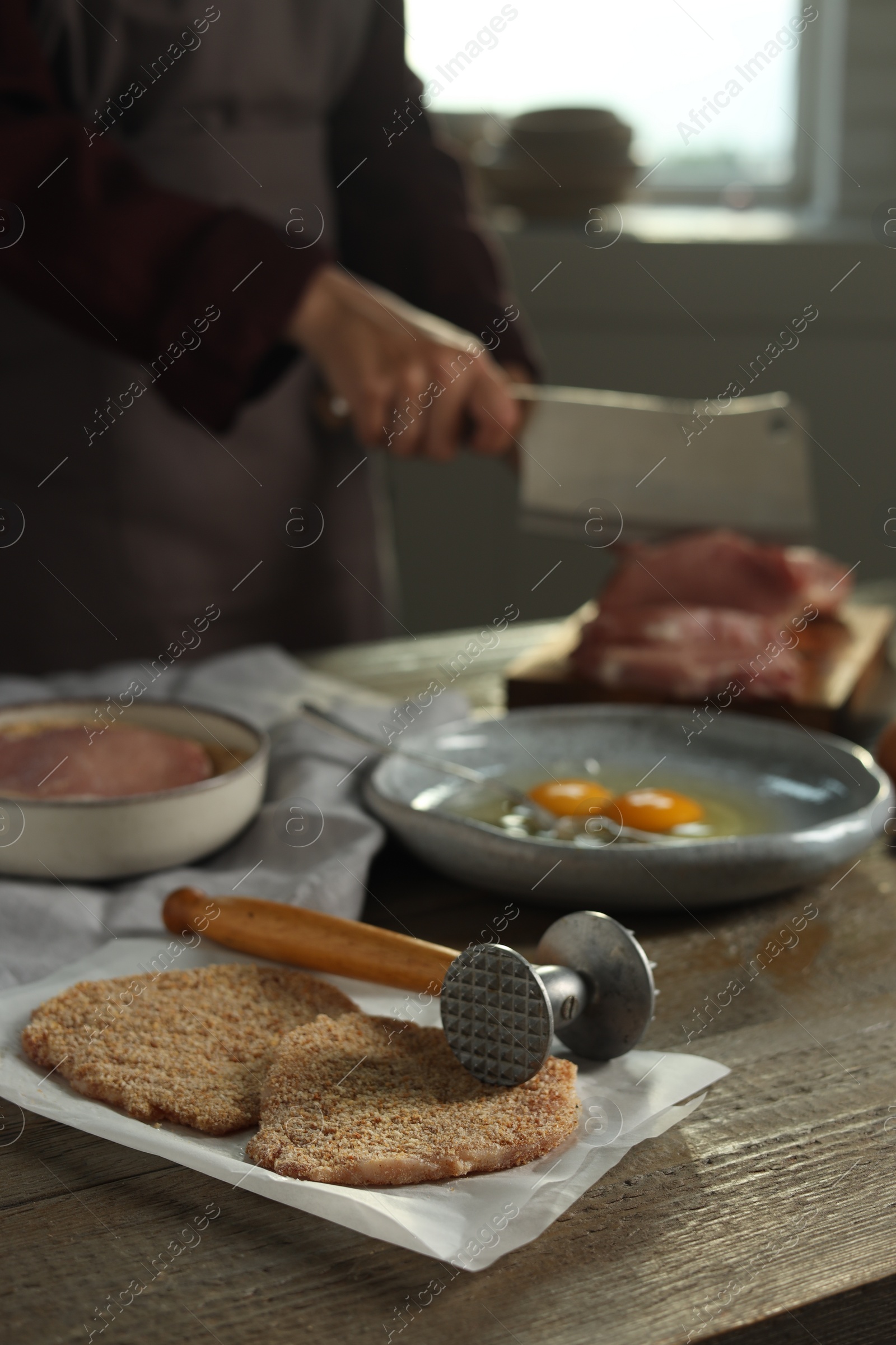 Photo of Woman cooking schnitzel at wooden table indoors, selective focus