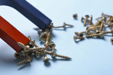 Photo of Magnet attracting screws on light blue background, closeup. Space for text