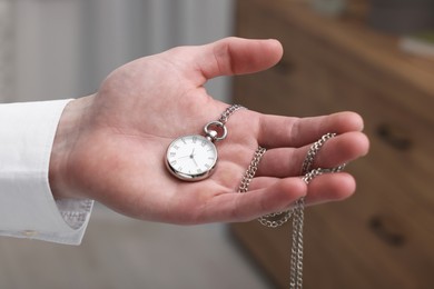 Photo of Man holding chain with elegant pocket watch on blurred background, closeup