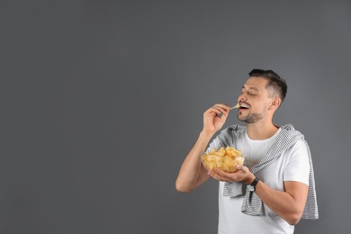 Photo of Man eating potato chips on grey background. Space for text