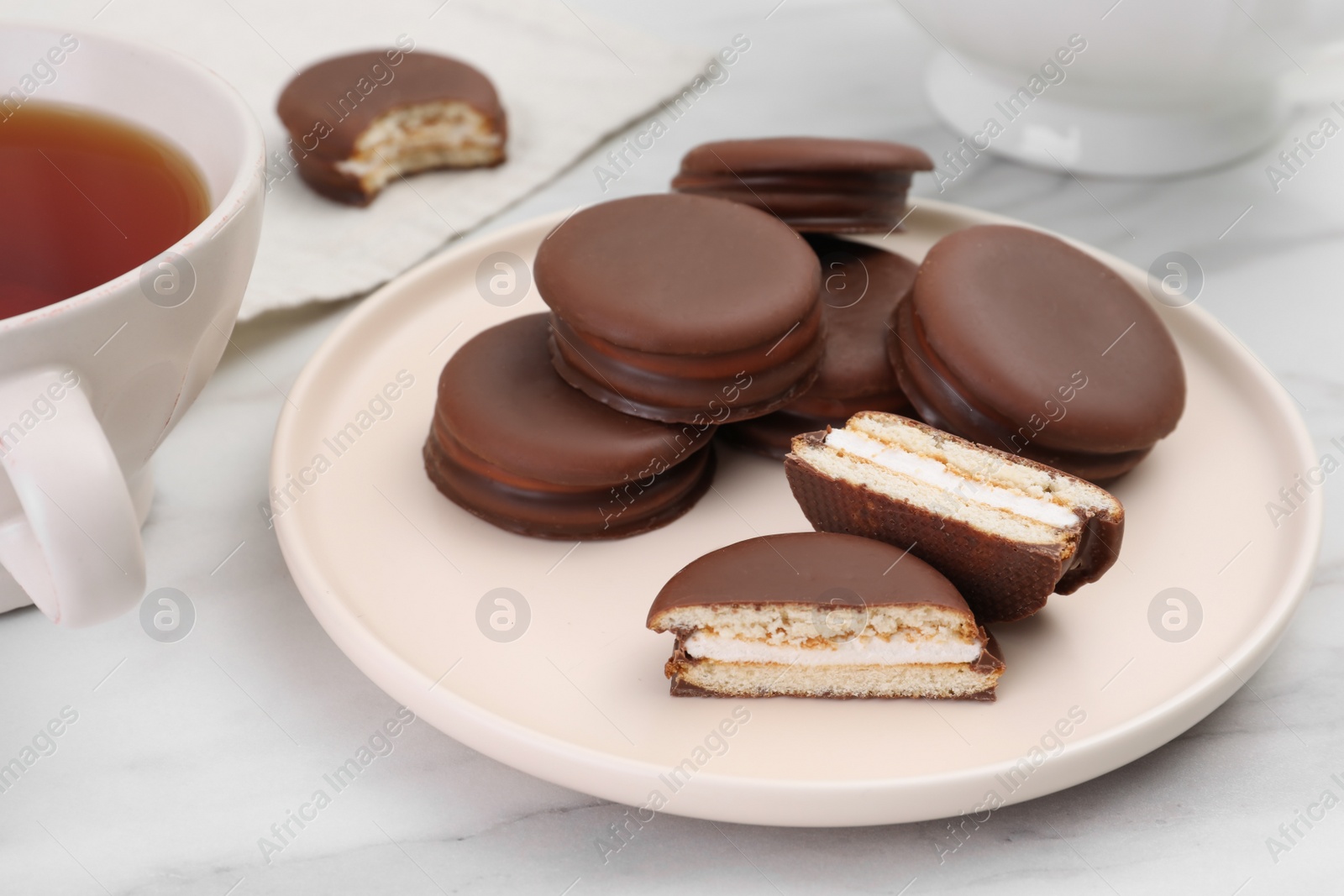 Photo of Plate with delicious choco pies and cup of tea on white marble table, closeup