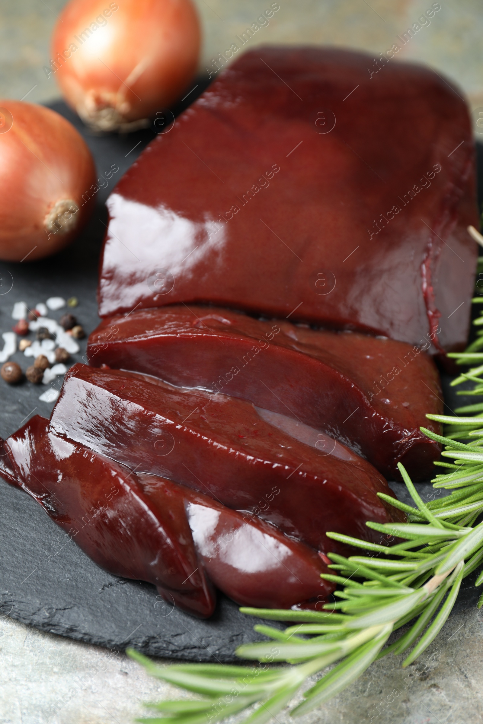 Photo of Cut raw beef liver with rosemary and onions on grey table, closeup