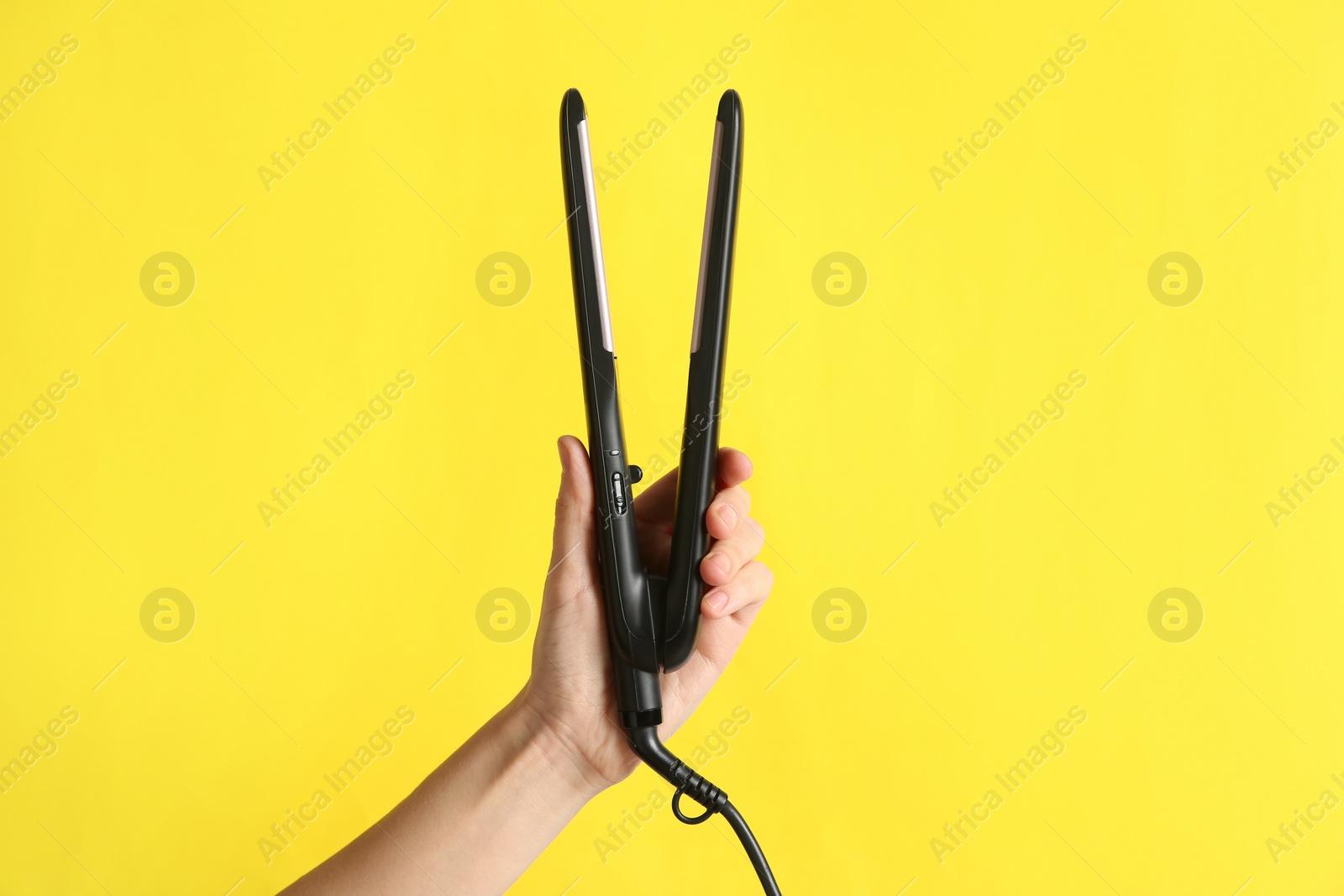 Photo of Woman holding flat hair iron on yellow background, closeup