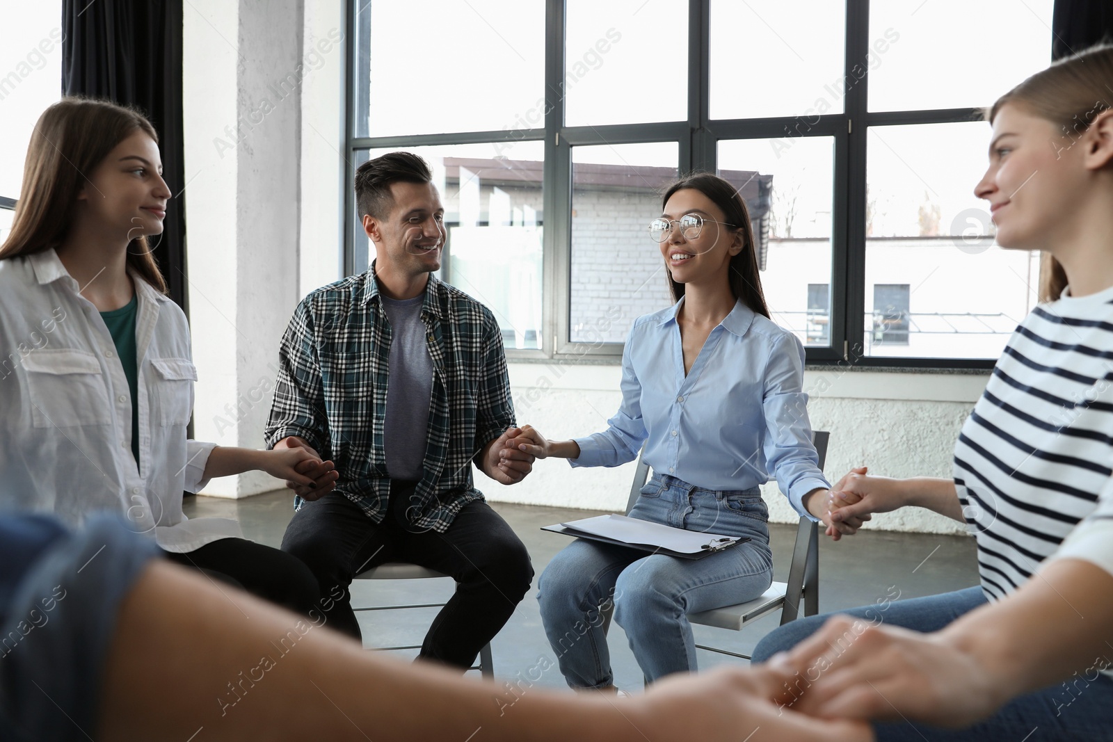 Photo of Psychotherapist holding hands with patients during group therapy session indoors