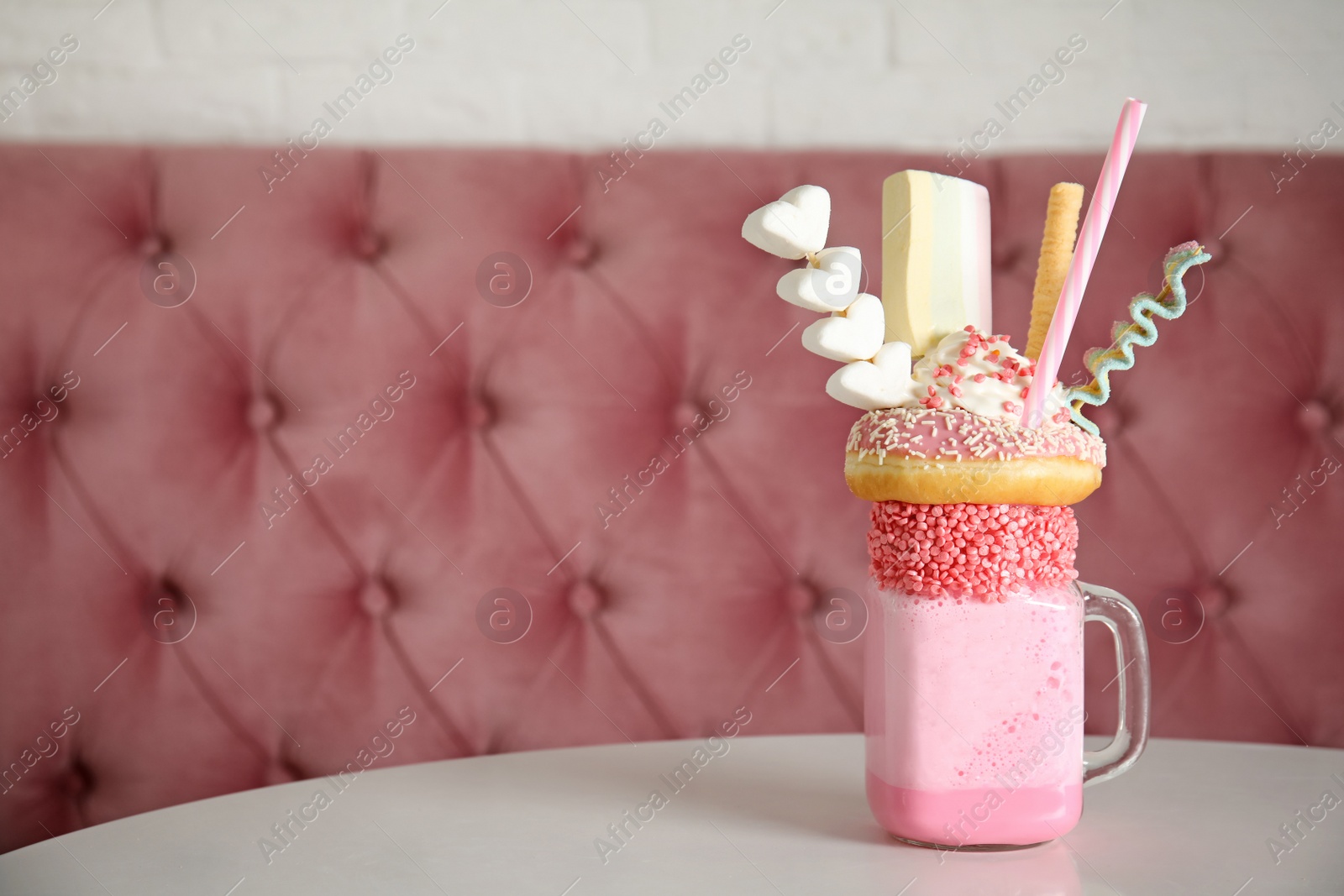 Photo of Tasty milk shake with sweets in mason jar on table at cafe. Space for text