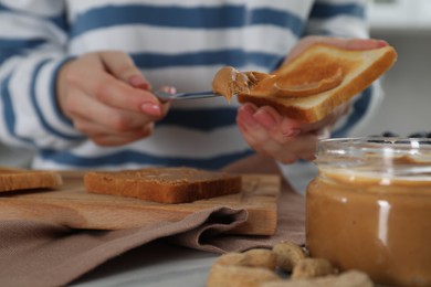 Woman with tasty nut butter on knife and toast at table, closeup