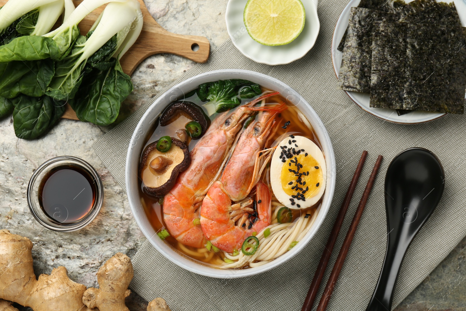 Photo of Delicious ramen with shrimps and egg in bowl served on grey textured table, flat lay. Noodle soup