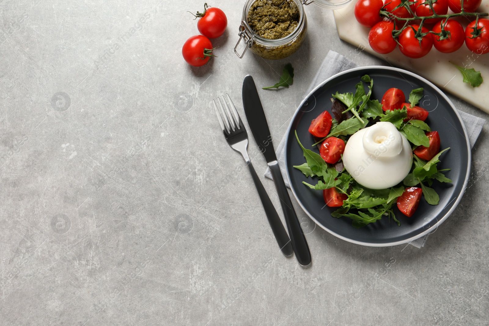 Photo of Delicious burrata salad with tomatoes and arugula served on grey table, flat lay. Space for text