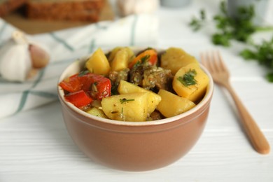 Photo of Tasty cooked dish with potatoes in earthenware served on white wooden table