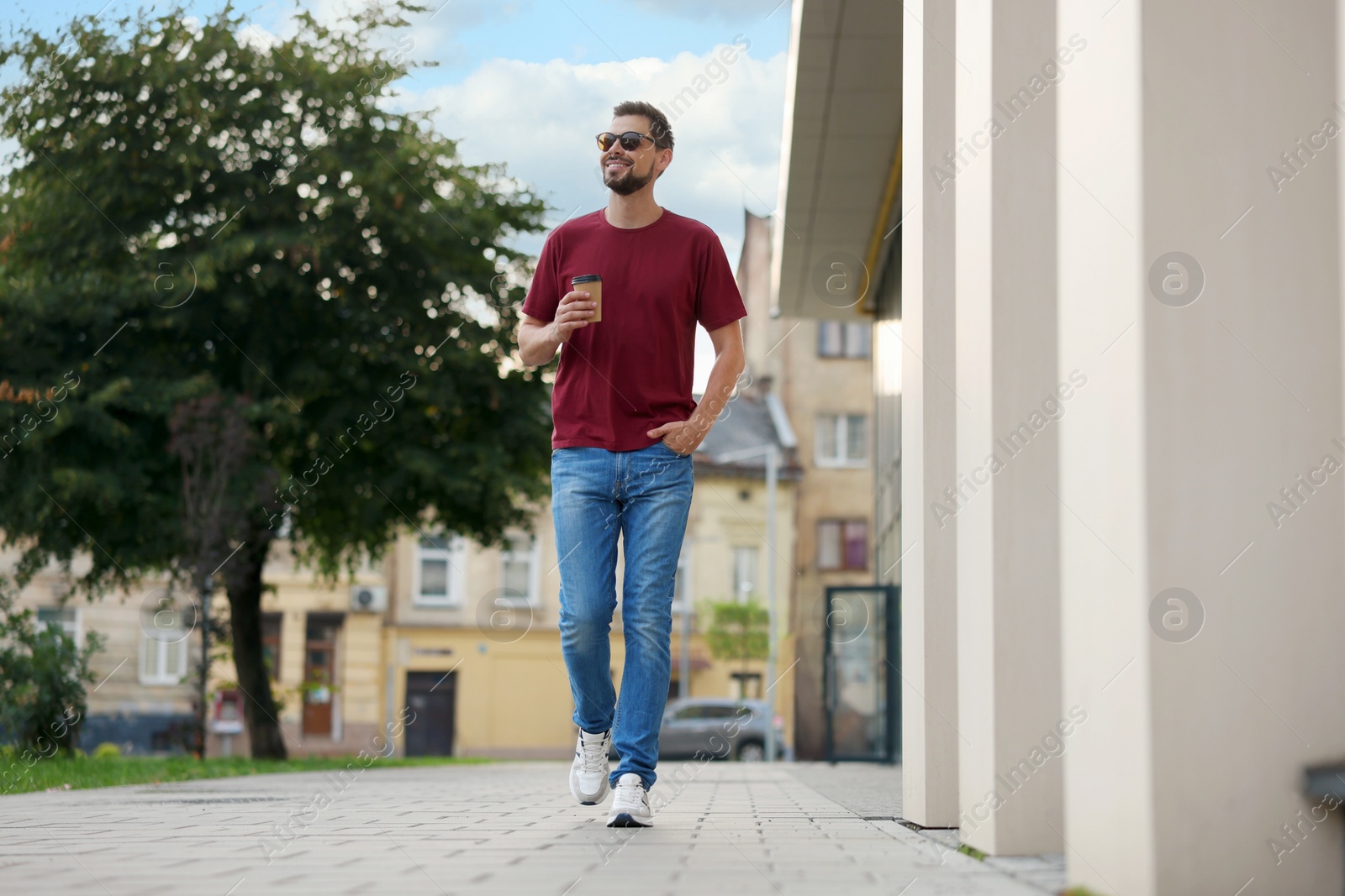 Photo of Handsome man with cup of drink walking on city street