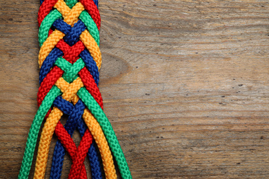 Photo of Top view of braided colorful ropes on wooden background, space for text. Unity concept