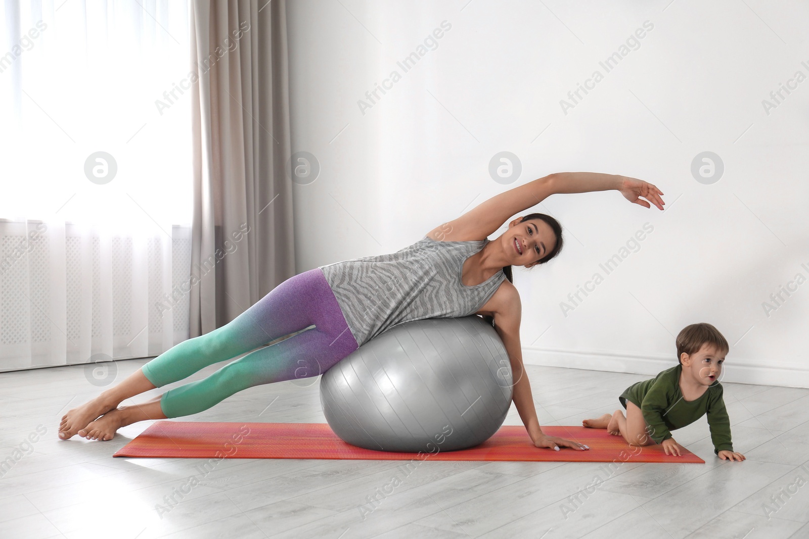 Photo of Young woman doing exercise with her son indoors. Home fitness