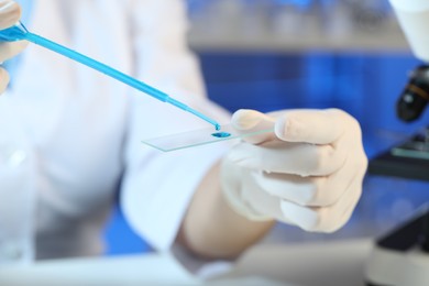 Scientist dripping sample of light blue liquid onto microscope slide in laboratory, closeup