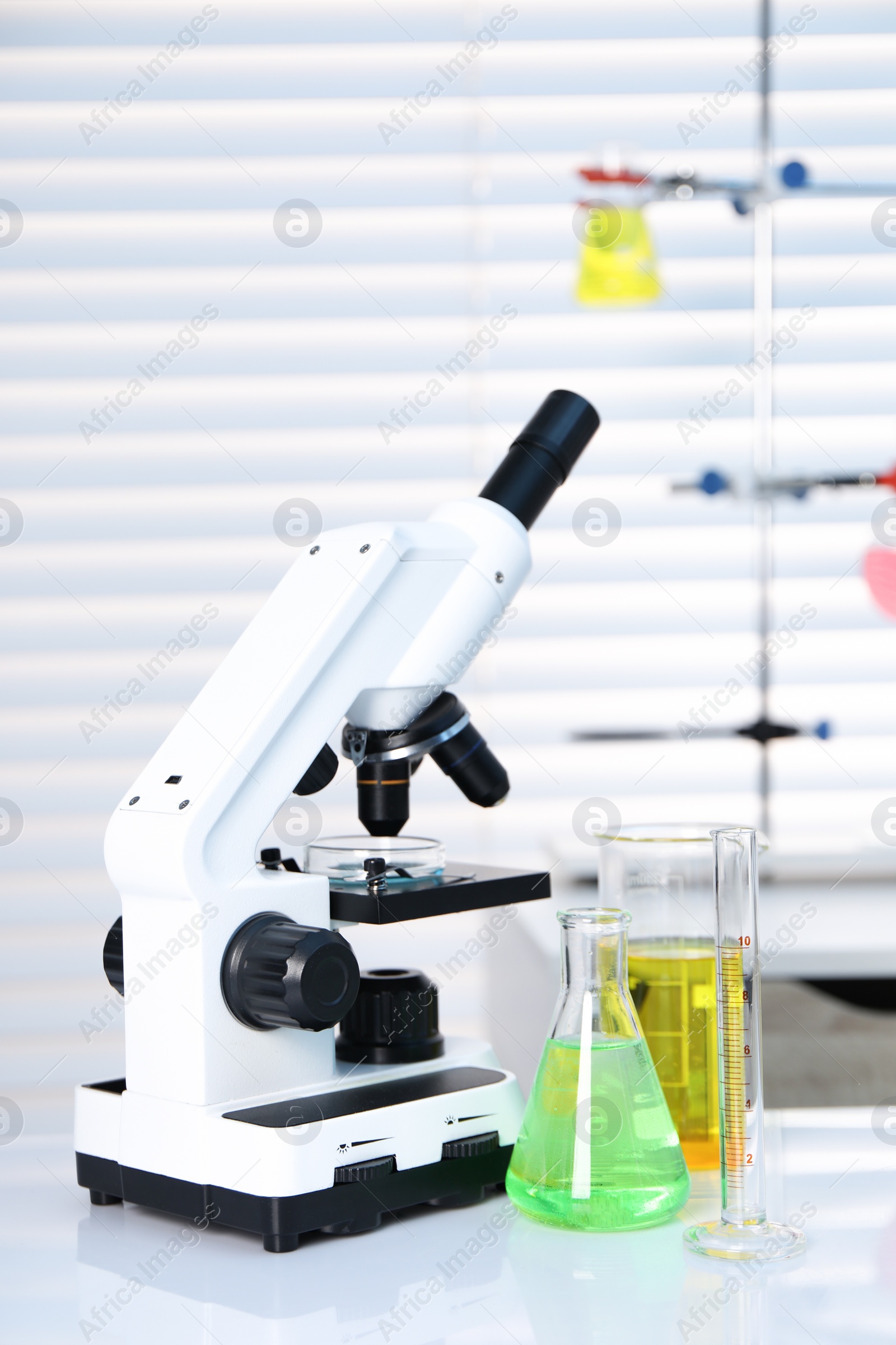 Photo of Laboratory analysis. Different glassware with liquids and microscope on white table indoors