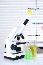 Photo of Laboratory analysis. Different glassware with liquids and microscope on white table indoors