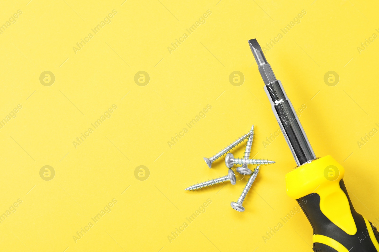 Photo of Screwdriver with black handle and screws on light yellow background, flat lay. Space for text