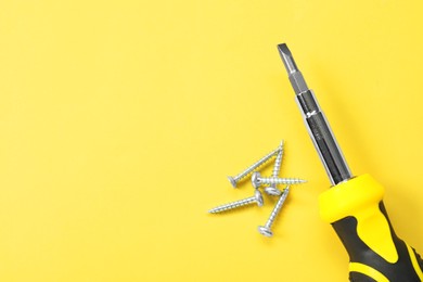 Photo of Screwdriver with black handle and screws on light yellow background, flat lay. Space for text