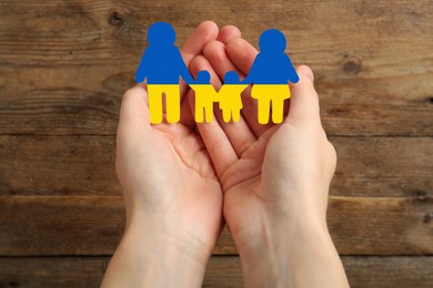Image of Woman holding paper family cutout in colors of Ukrainian flag on wooden background, closeup