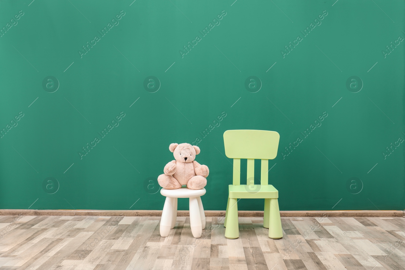 Photo of Stuffed toy bear on stool and chair in child room. Space for text