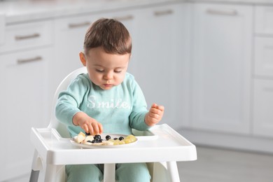 Cute little baby eating healthy food in high chair at home. Space for text